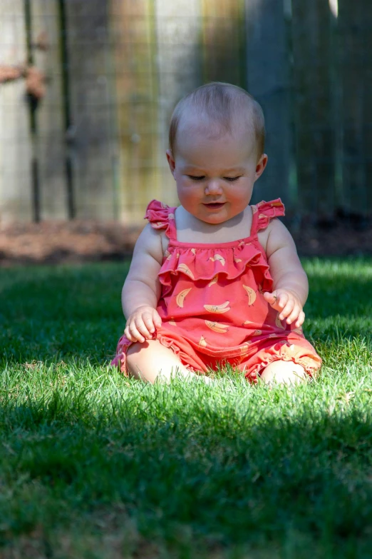 a baby sitting on top of a lush green field, red jumpsuit, in the yard, with a lush grass lawn, zoomed in