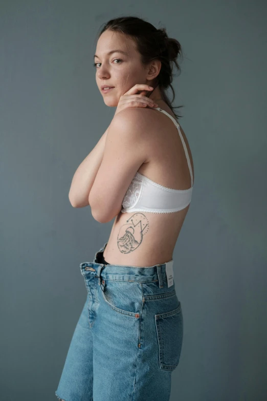 a woman with a tattoo on her back, trending on pexels, hand on hips, plain background, an anthropomorphic stomach, 18 years old