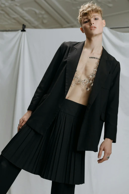 a man in a black suit standing in front of a white backdrop, an album cover, by Caro Niederer, trending on pexels, renaissance, pleated skirt, bralette, photo of a hand jewellery model, wearing fashion suit