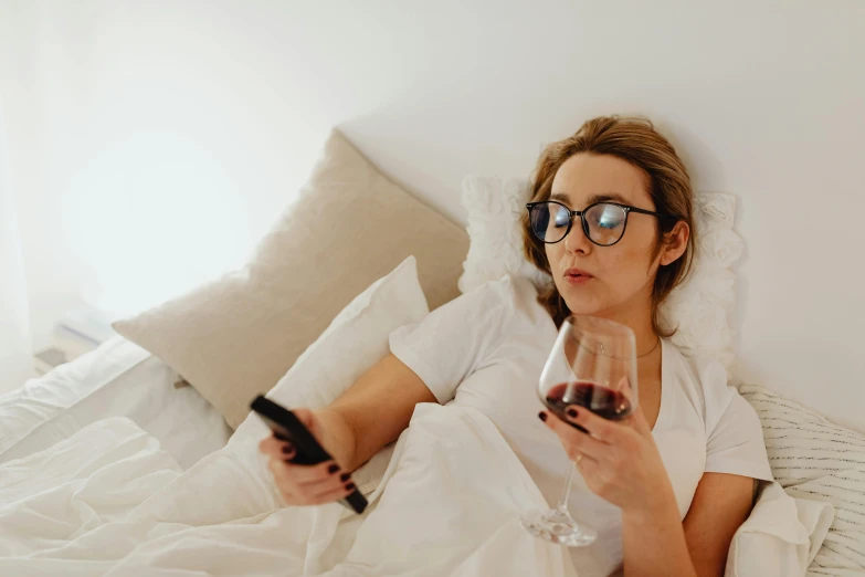 a woman laying in bed with a glass of wine, trending on pexels, happening, watching tv, with glasses, full-body, instagram photo