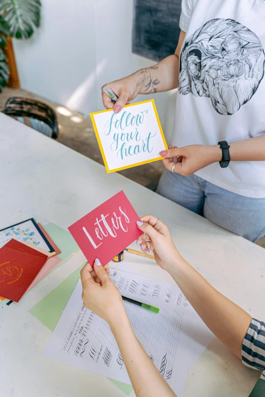 a couple of people that are holding some cards, a silk screen, trending on unsplash, letterism, in a workshop, instagram story, colorful signs, writing a letter