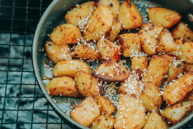 a pan filled with cooked potatoes on top of a grill, by Daniel Lieske, unsplash, mingei, luscious with sesame seeds, 1980s photo, fan favorite, tribbles