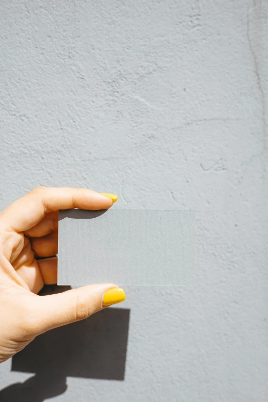 a person holding a business card in their hand, by Kristian Zahrtmann, pexels contest winner, postminimalism, light grey blue and golden, made of cement, woman, cmyk