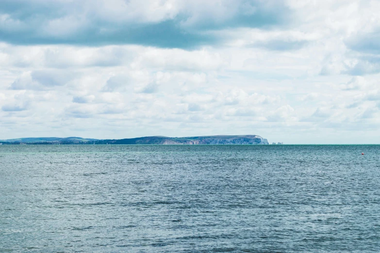 a large body of water under a cloudy sky, by Rachel Reckitt, unsplash, seaview, high cliff, clear skies in the distance, seen from a distance