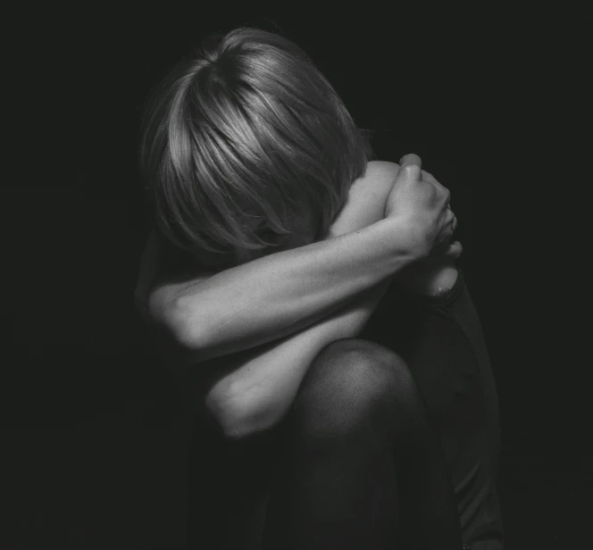 a black and white photo of a woman covering her face with her hands, by Emma Andijewska, hugging her knees, what depression looks like, young child, black background pinterest