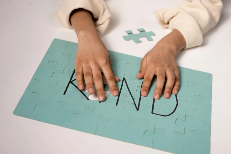 a person holding a puzzle piece with the word kind written on it, trending on pexels, interactive art, kid a, penned in cyan ink, knolling, face down