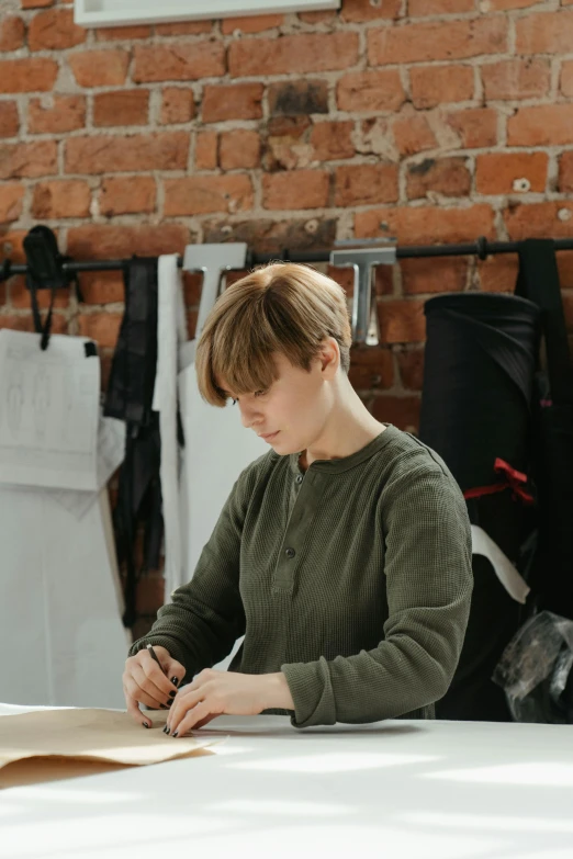 a woman sitting at a table writing on a piece of paper, by Ilya Ostroukhov, pexels contest winner, arbeitsrat für kunst, wearing a designer top, leather padding, inspect in inventory image, androgynous person