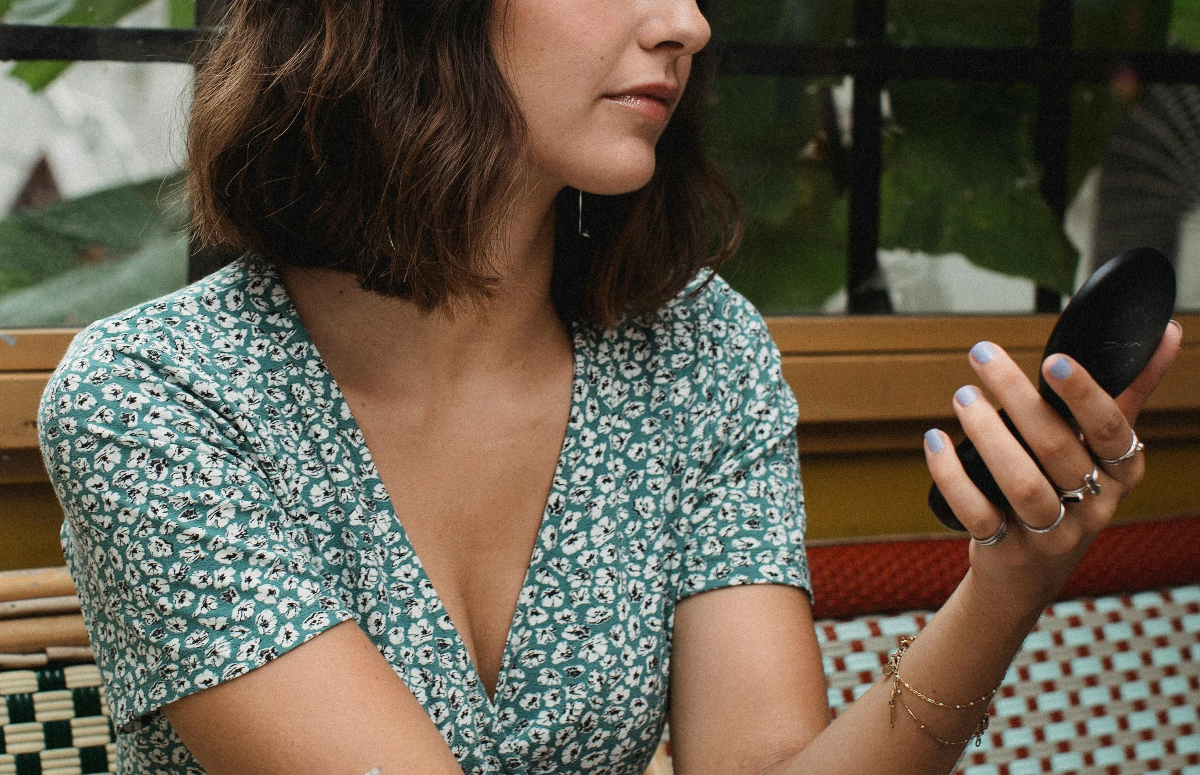 a woman sitting at a table with a cell phone, trending on pexels, figuration libre, floral patterned skin, background image, wearing v - neck top, abcdefghijklmnopqrstuvwxyz