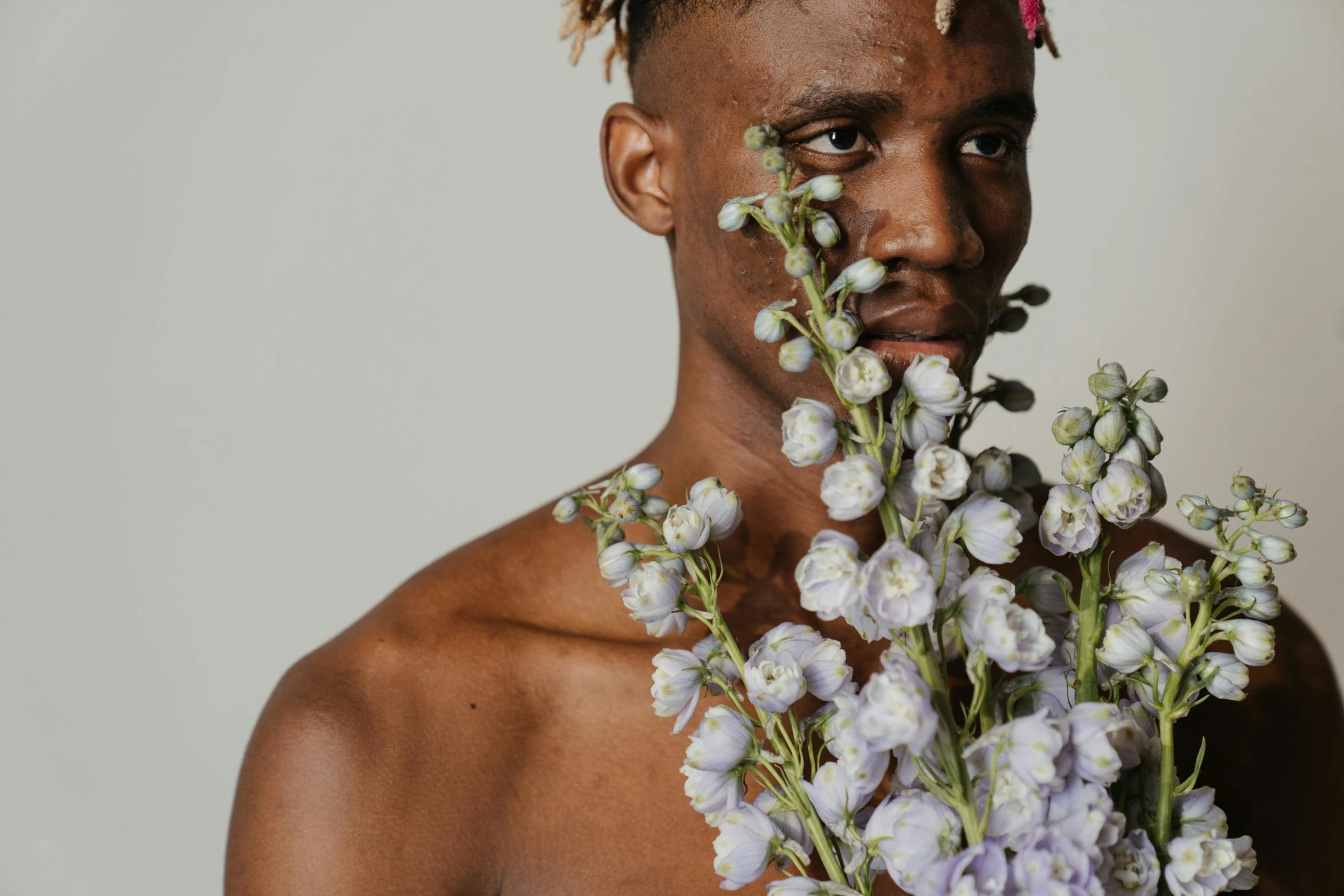 a man with dreadlocks holding a bunch of flowers, inspired by Xanthus Russell Smith, trending on pexels, delicate androgynous prince, with brown skin, travis scott, attractive photo