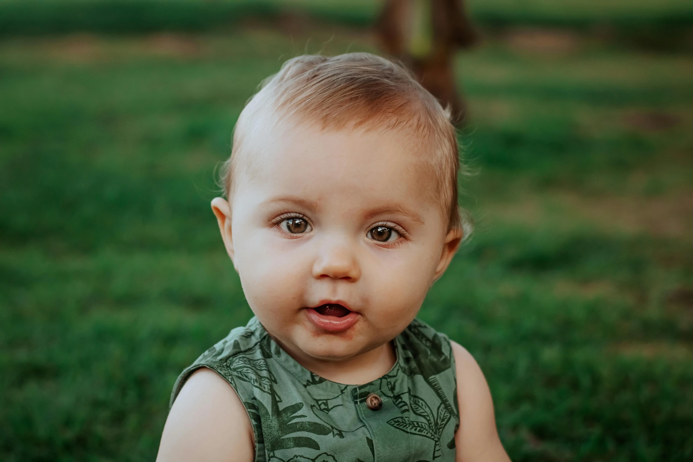 a baby sitting on top of a lush green field, pexels contest winner, photorealism, handsome face, patterned, lachlan bailey, very shallow depth of field