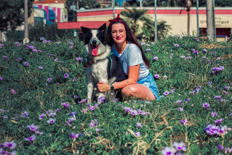 a woman sitting in a field of purple flowers with her dog, a colorized photo, pexels contest winner, border collie, in a city park, avatar image, smiling at camera