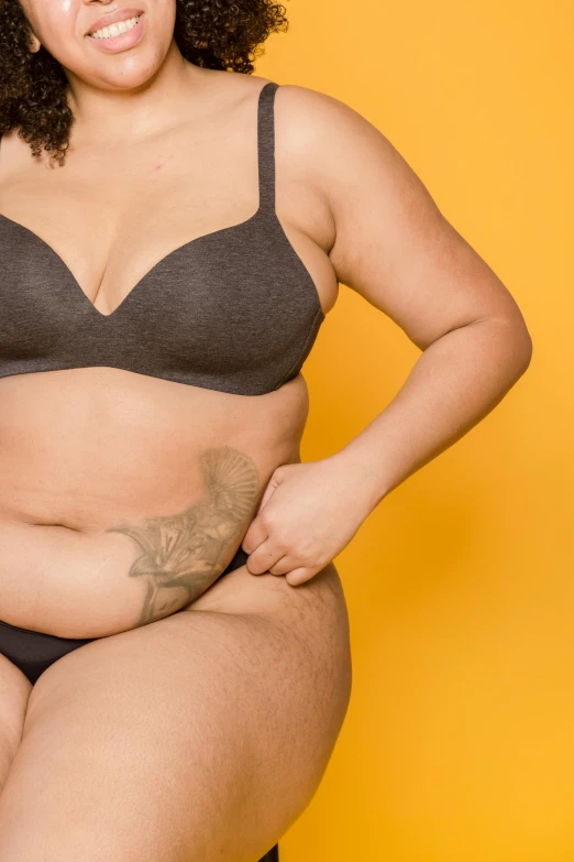 a woman in a black bra top sitting on a stool, trending on pexels, her belly is fat and round, photograph of a sleeve tattoo, yellow skin, an anthropomorphic stomach