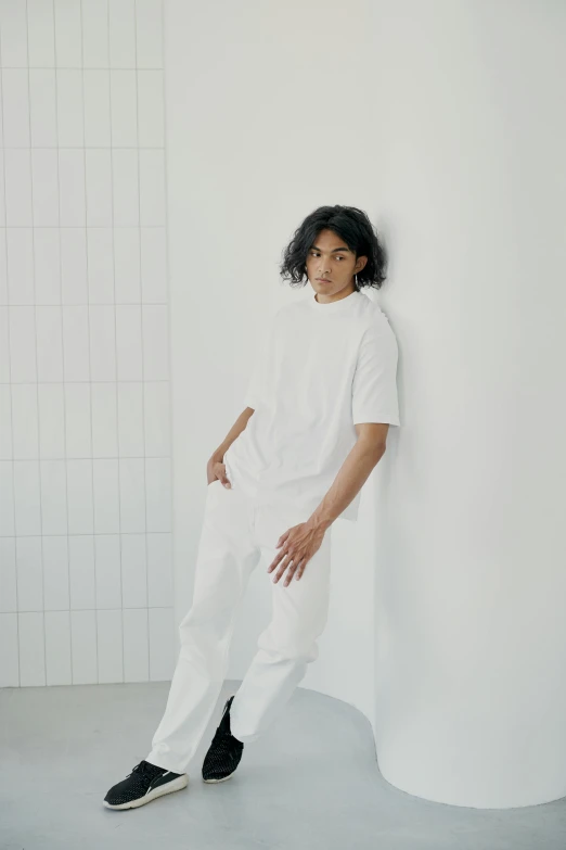 a man leaning against a wall in a white room, trending on unsplash, happening, wearing white clothes, non binary model, yuya nagai, wearing pants and a t-shirt