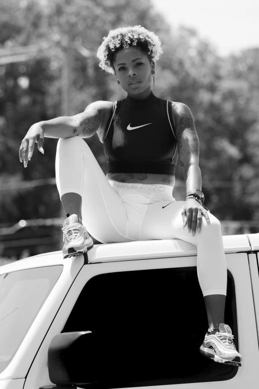 a black and white photo of a woman sitting on top of a car, athletic and strong, kezie demessance, square, justify