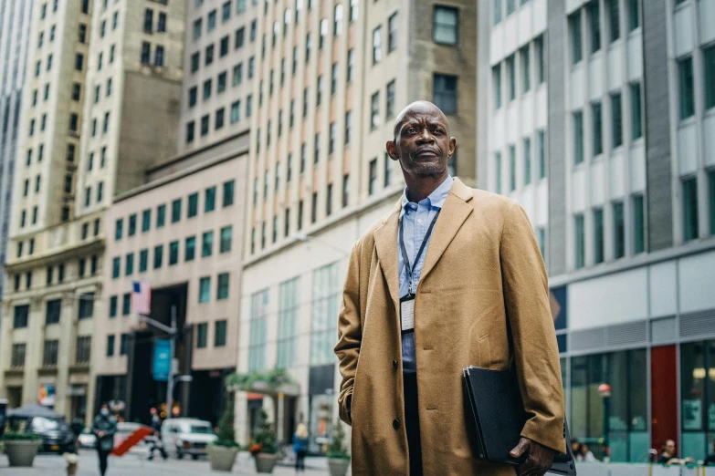 a man standing in the middle of a city street, by William Berra, pexels contest winner, lance reddick, older male, he wears a big coat, highrise business district