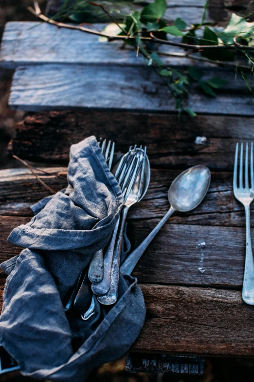 a bunch of silverware sitting on top of a wooden table, a still life, unsplash, multiple stories, eating outside, rustic and weathered, blue