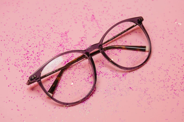 a pair of glasses sitting on top of a pink surface, purple sparkles, black rimmed glasses, glasses |, fan favorite