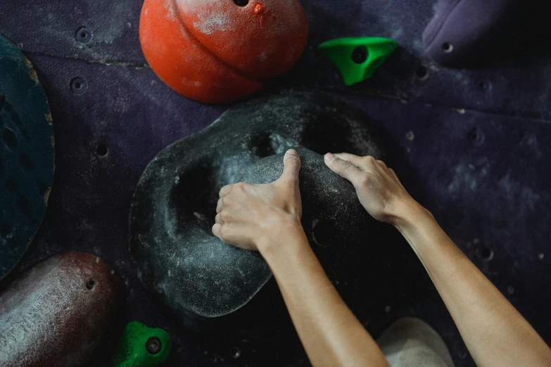 a close up of a person climbing on a wall, rounded shapes, hand holding cap brim, in a planet fitness, ((rocks))