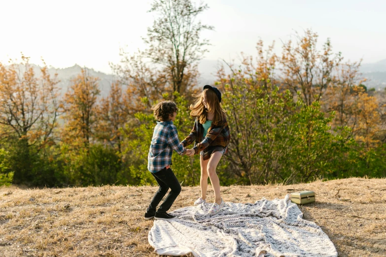 a couple of kids standing on top of a blanket, by Jessie Algie, pexels contest winner, couple dancing, having a picnic, on ground, promotional image