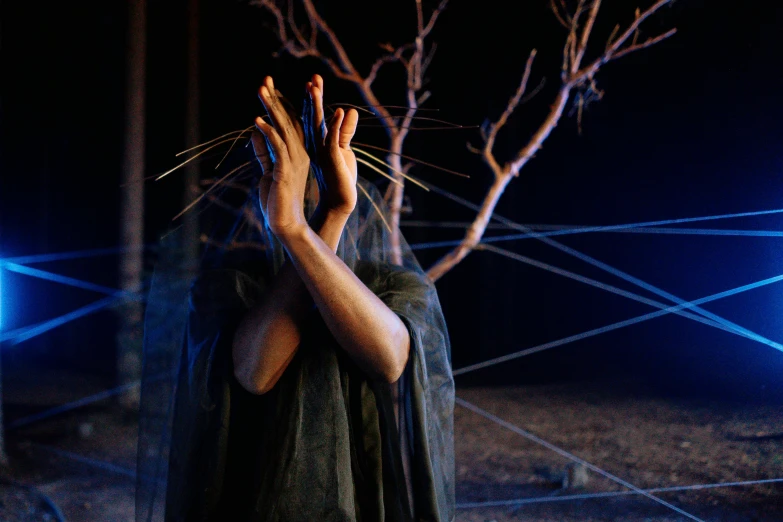 a woman in a black dress covering her face with her hands, a surrealist sculpture, by Hannah Tompkins, unsplash, conceptual art, with screens and silks, the spider thicket, aboriginal capirote, man holding spear