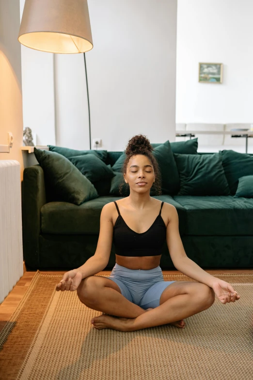 a woman sitting on a rug in a living room, trending on pexels, meditating in lotus position, green aura, low quality photo, ashteroth