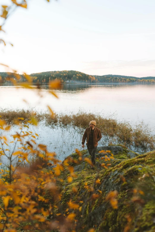 a man standing on top of a lush green hillside next to a lake, by Eero Järnefelt, fall foliage, walking towards camera, golden glow, camp