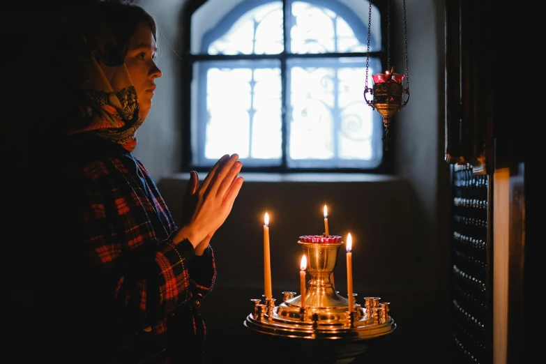 a woman standing in front of a lit candle, by Julia Pishtar, pexels, renaissance, in orthodox church, instagram post, praying, slavic style