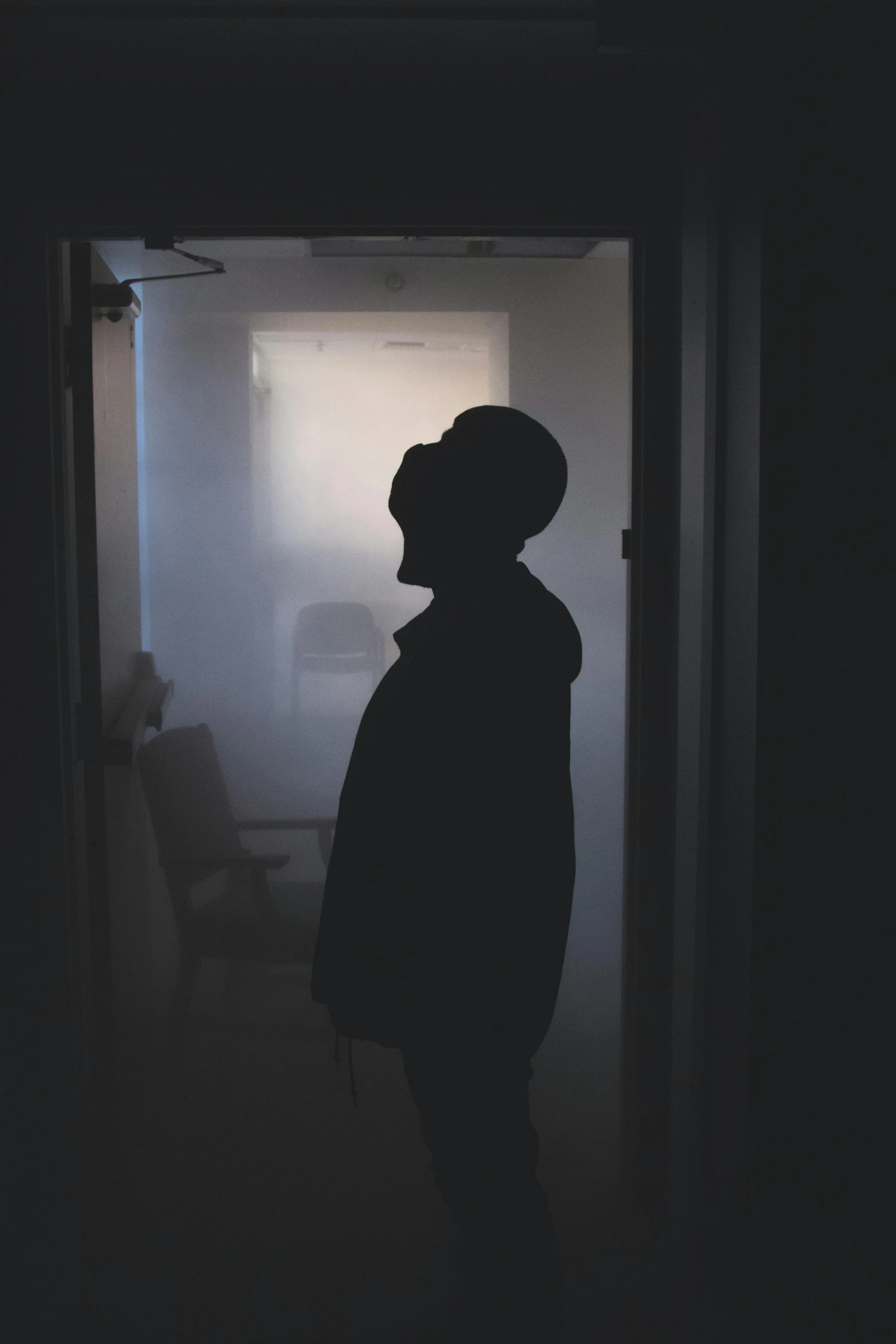 a silhouette of a person standing in a dark room, by Ryan Pancoast, dark visor covering face, in a foggy office, teenage boy, stood in a lab