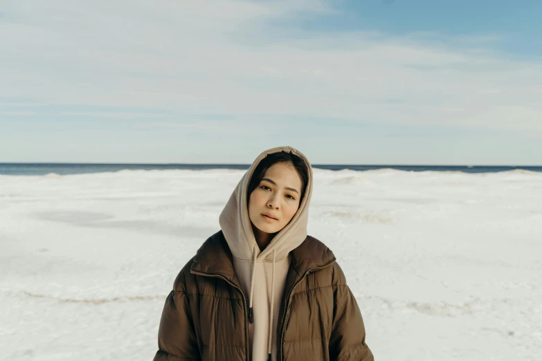 a woman standing on top of a snow covered beach, inspired by Kim Tschang Yeul, trending on pexels, hyperrealism, beige hoodie, young cute wan asian face, **cinematic, finland