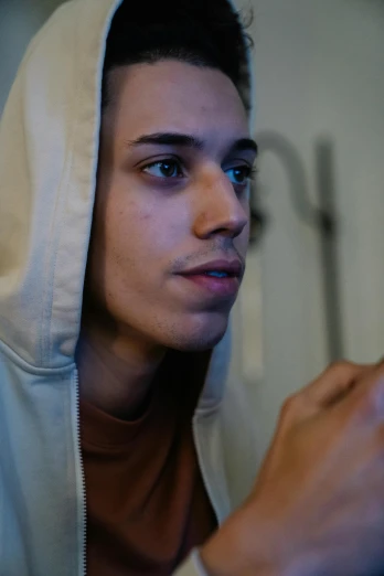 a close up of a person holding a cell phone, by Jacob Toorenvliet, beige hoodie, young spanish man, looking in mirror, color footage