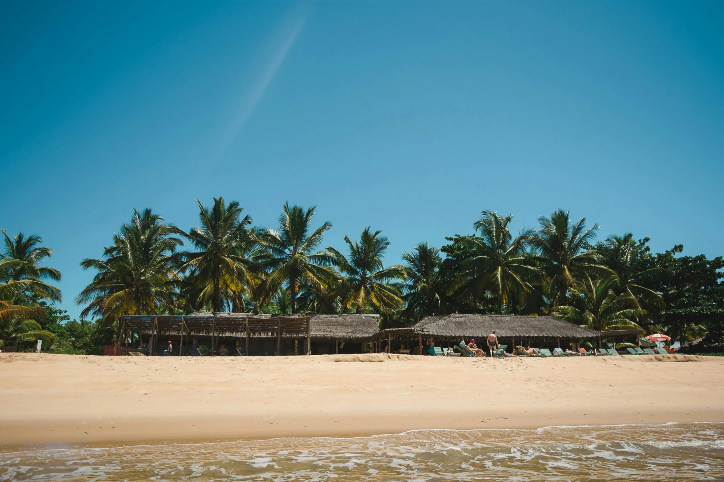 a couple of huts sitting on top of a sandy beach, profile image, palm trees, clear blue skies, crowded beach