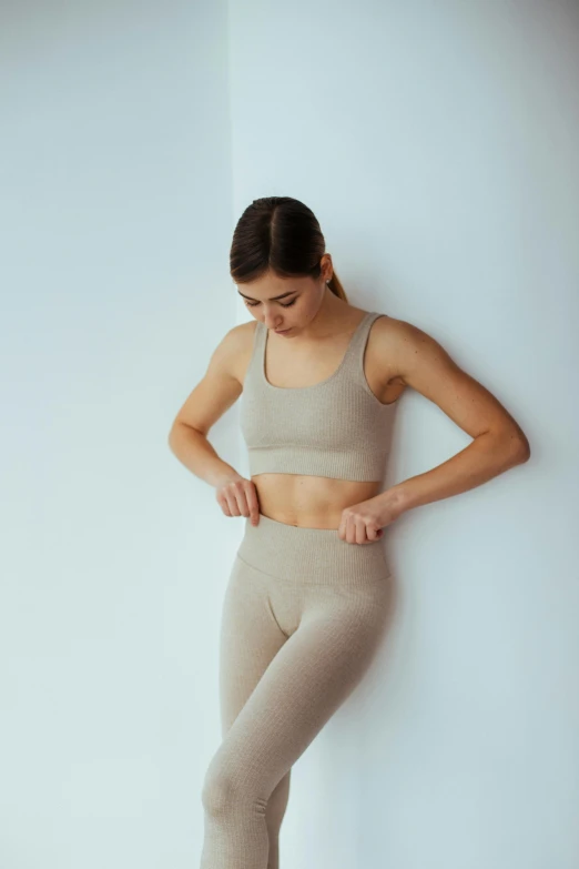 a woman leaning against a wall with her hands on her hips, trending on pexels, taupe, detailed sports bra, sustainable materials, met collection