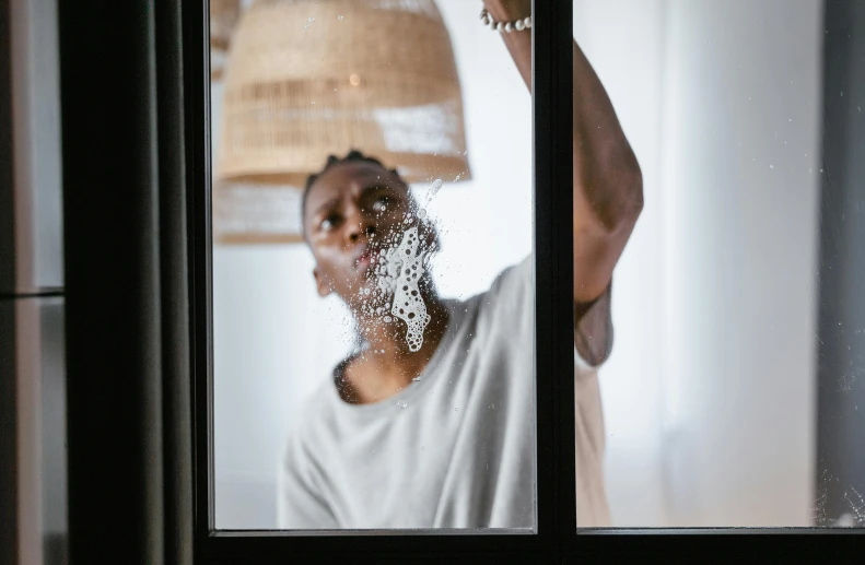 a man shaving his face in front of a window, pexels contest winner, visual art, black teenage boy, bubbles in the air, hanging from white web, maintenance