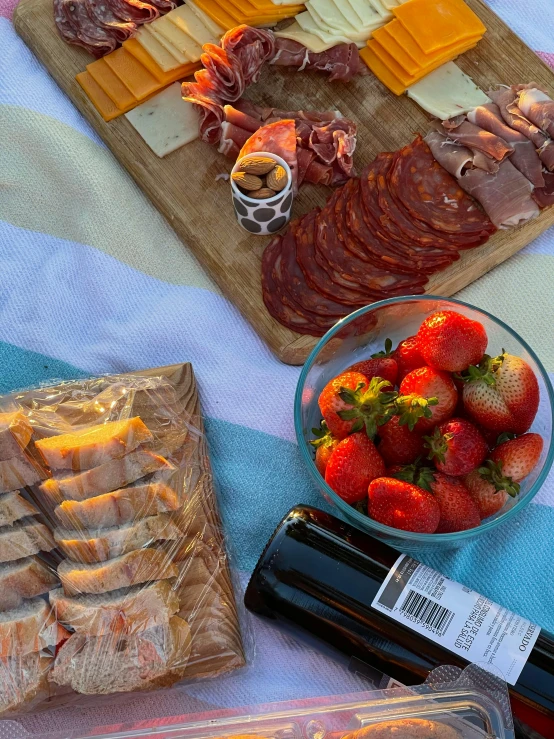 a table topped with lots of food next to a bottle of wine, a picture, next to sliced strawberries, chorizo sausage, summer sky, 6 pack