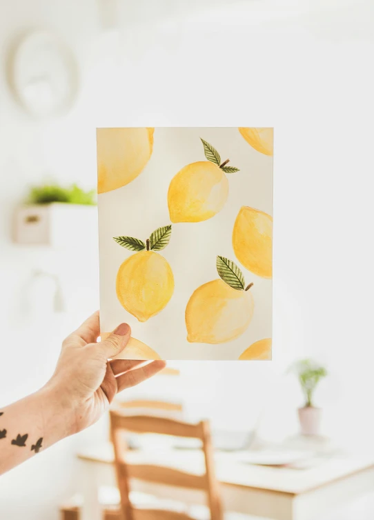 a person holding up a piece of paper with lemons on it, poster art, by Julia Pishtar, trending on pexels, nursery poster, glossy surface, greeting card, kitchen background