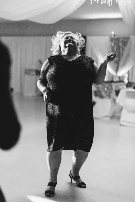 a black and white photo of a woman on a dance floor, a black and white photo, unsplash, obese, laughter, wearing a black dress, running towards camera