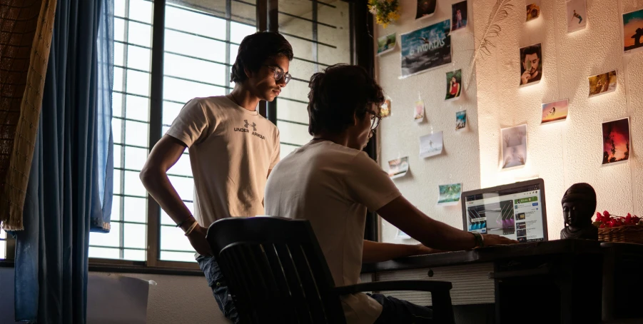 a couple of people sitting at a table with a laptop, by Max Dauthendey, pexels contest winner, process art, standing in corner of room, in sci - fi mumbai, two young men, college students