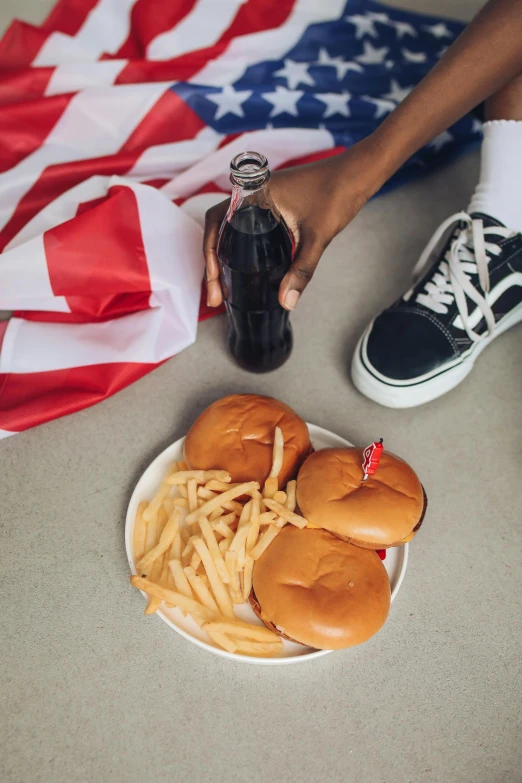 a person sitting on the ground with a plate of food and a bottle of soda, american flags, addidas, gen z, french fries