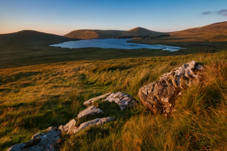 a large body of water sitting on top of a lush green hillside, by Peter Churcher, pexels contest winner, land art, orkney islands, morning golden hour, mountain lakes, youtube thumbnail