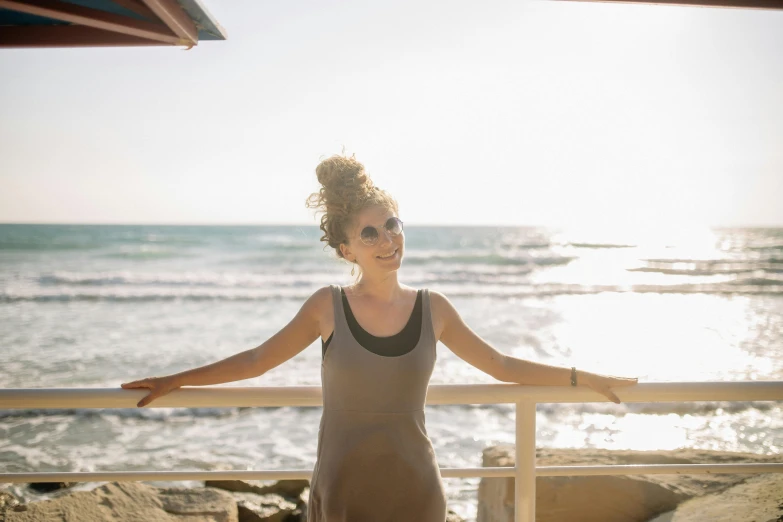 a woman standing on top of a beach next to the ocean, beachwood treehouse, profile image, avatar image, warm glow