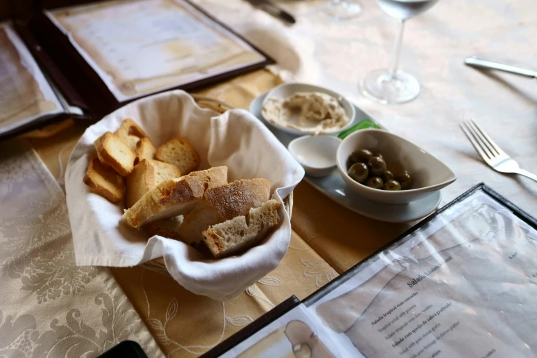 a bowl of bread sitting on top of a table, olives, restaurant, with bread in the slots, thumbnail