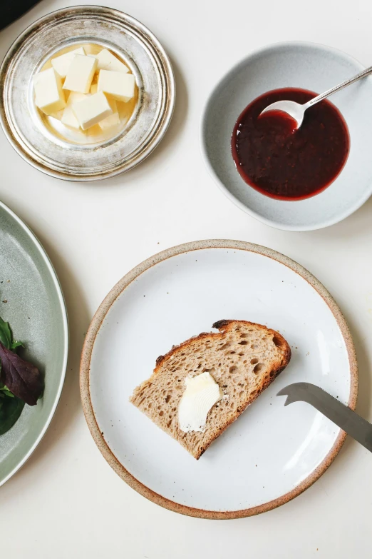 a white table topped with plates of food, a still life, inspired by Richmond Barthé, unsplash, brown bread with sliced salo, hammershøi, maroon, butter