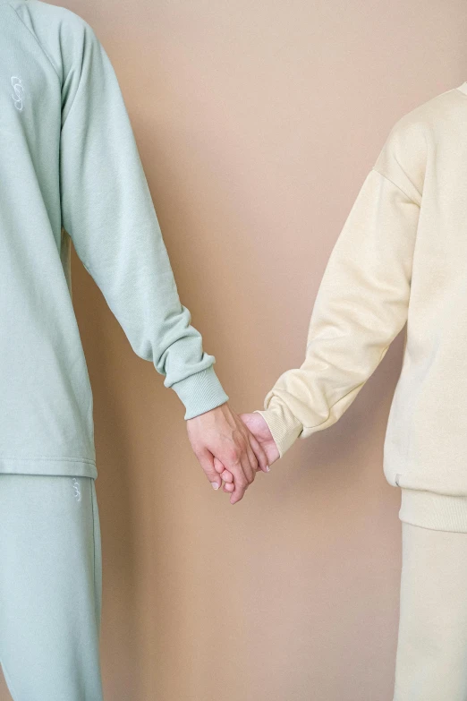 a man and a woman holding hands in front of a wall, a colorized photo, by Nina Hamnett, trending on unsplash, sleepwear, pastel green, beige, wearing sweatshirt