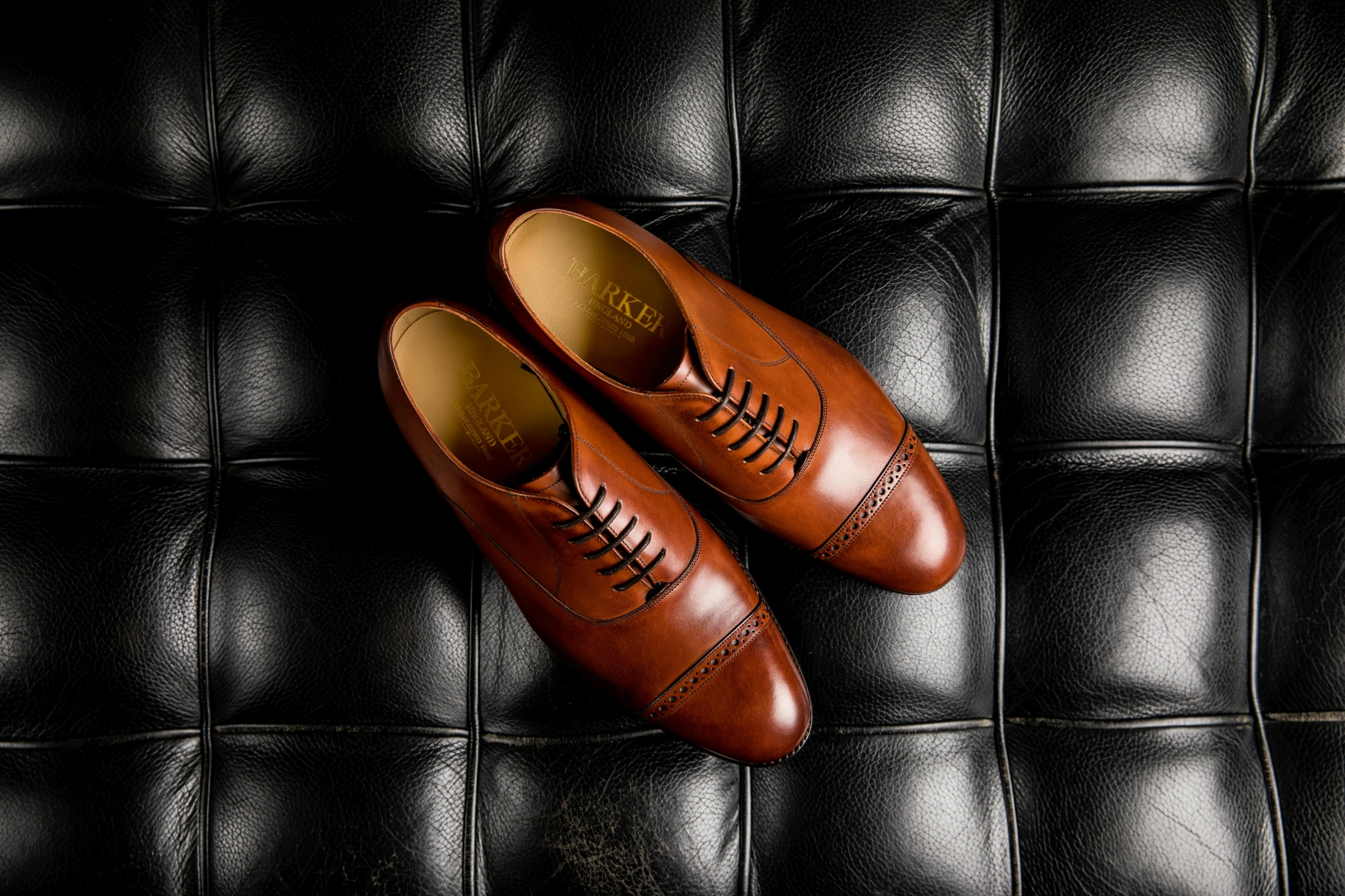 a pair of brown shoes sitting on top of a black leather couch, inspired by Alfred Janes, instagram, smooth panelling, taking from above, commissioned, looking across the shoulder