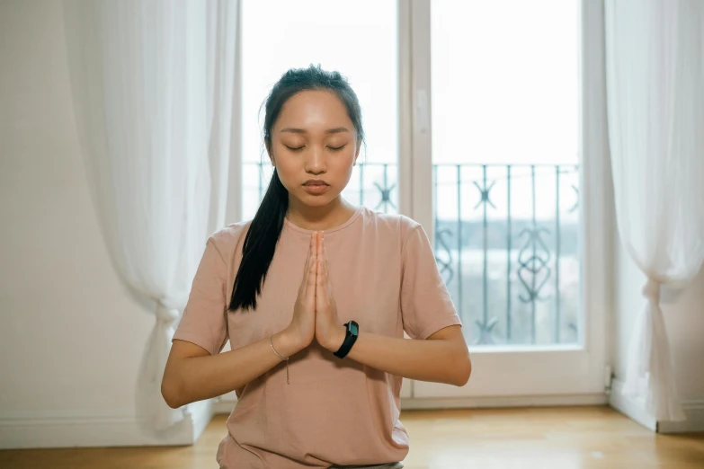 a woman sitting in a yoga position in front of a window, inspired by Ruth Jên, trending on pexels, hurufiyya, partially cupping her hands, a young asian woman, praying, slightly pixelated