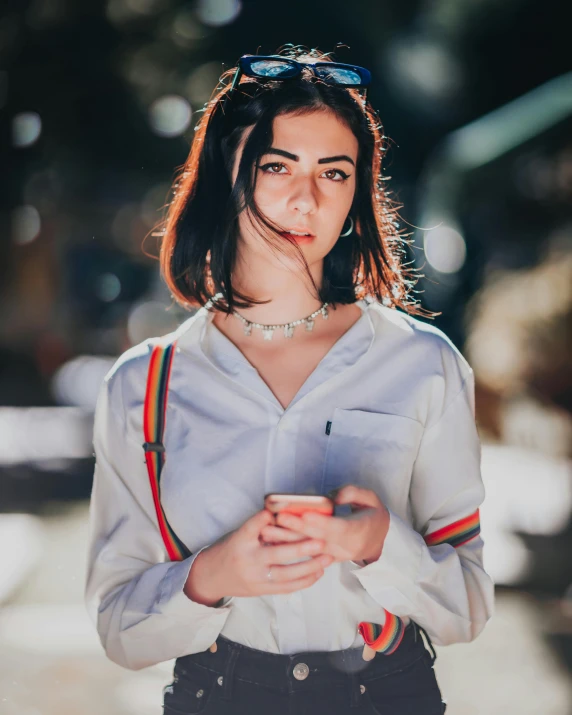 a woman standing on a street holding a cell phone, inspired by Elsa Bleda, trending on pexels, pale-skinned persian girl, collared shirt, multicoloured, portrait mode photo