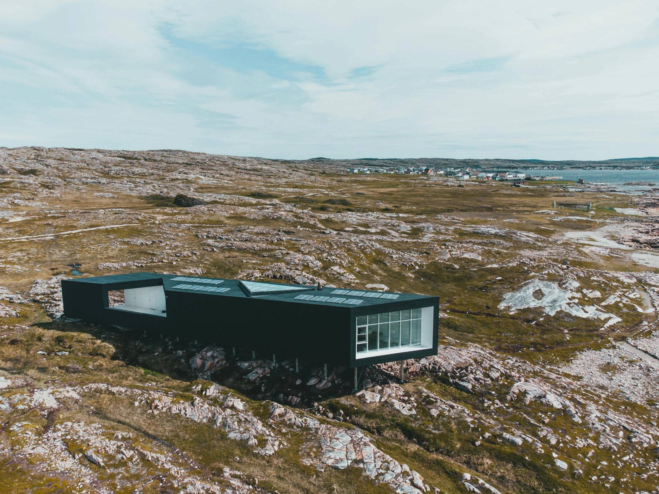 a house sitting on top of a hill next to a body of water, by Jesper Knudsen, pexels contest winner, black steel buildings, inuit, looking down on the camera, iconic design