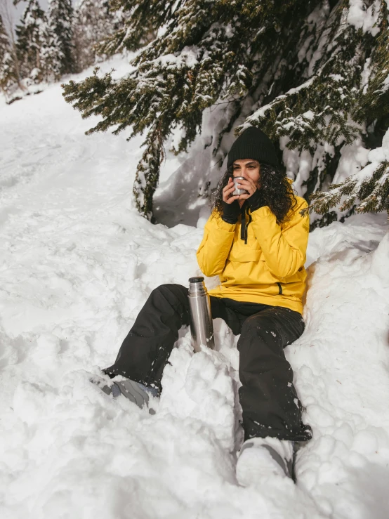 a woman in a yellow jacket is sitting in the snow, pexels contest winner, taking a smoke break, wearing adventure gear, avatar image, holding a drink