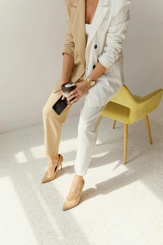 a woman sitting on top of a yellow chair, inspired by Eva Gonzalès, trending on pexels, minimalism, tan suit, iced latte, shoes, subtle textures