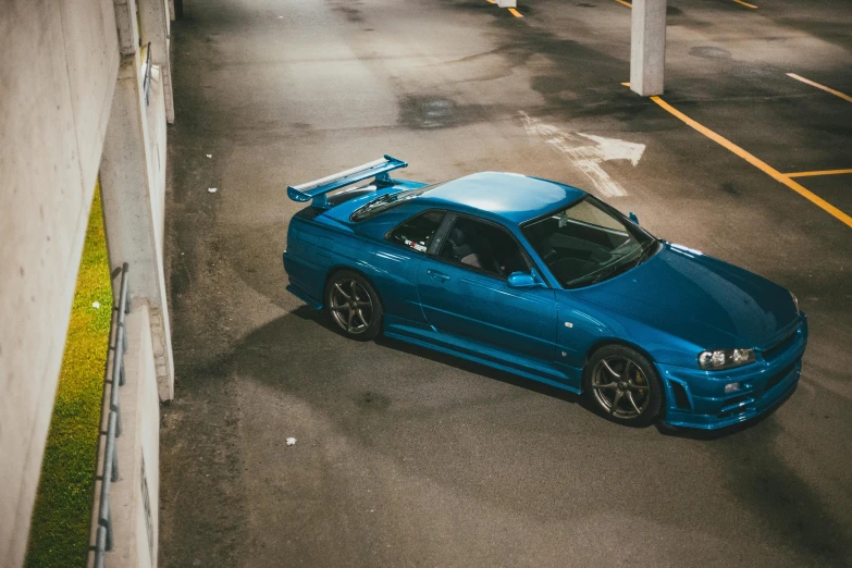 a blue car parked in a parking lot, inspired by Kanō Hōgai, pexels contest winner, in a modified nissan skyline r34, lit from above, new zealand, on the concrete ground